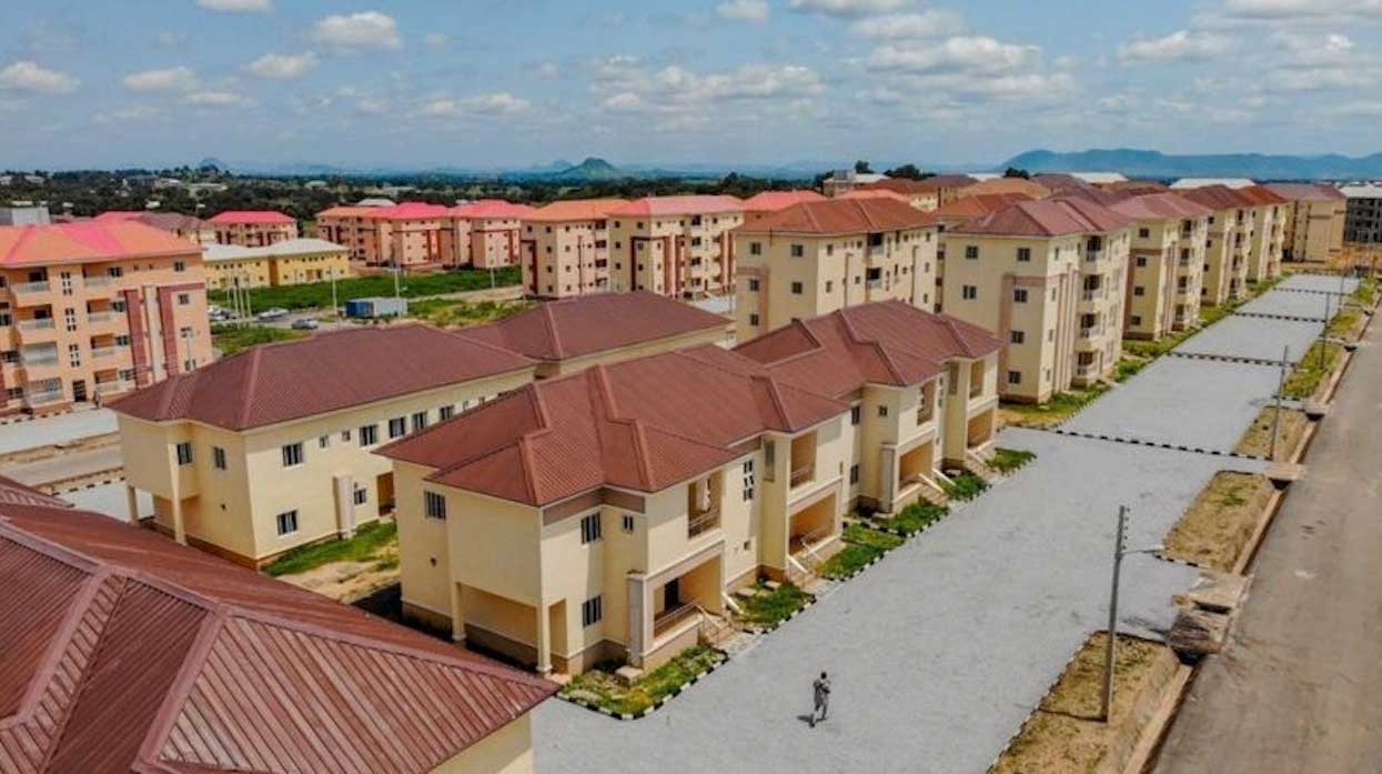Aerial view of dense urban housing in Lagos Nigeria showing informal settlements alongside unfinished construction projects illustrating the scale of the housing affordability crisis